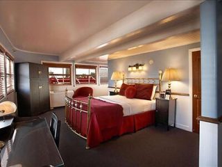A luxuriousn bedroom with a large, comfortable bed draped in a red bedspread, elegant lighting, and windows providing a view
